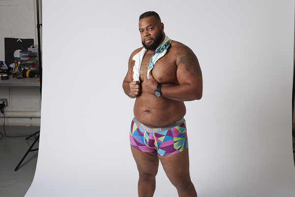 African American gay bear model wears Play Out underwear and holds shirt over his shoulders.